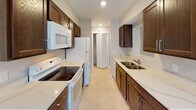 Located at 1101 Kusterer Dr NW in Walker, Michigan, this single-floor unit offers a well-organized layout designed for comfortable everyday living. The galley-style kitchen is a functional highlight, featuring rich dark wood cabinetry, light-toned countertops, and a full suite of white appliances including an electric range, over-the-range microwave, refrigerator, and dishwasher. A double basin sink is positioned along one wall, and a bi-fold door at the end of the kitchen provides access to additional storage. The open living area is carpeted and benefits from multiple windows that allow natural light to fill the space, along with a glass door offering outdoor access and views of the surrounding greenery. A pass-through window connects the living area to the kitchen, enhancing the sense of openness. The bedrooms are carpeted and simply finished with neutral walls, recessed lighting, and windows overlooking the outdoors. Baseboard heating units are present in several rooms. The bathroom includes a full tub and shower combo with a clean white surround, a toilet, and light tile flooring. Throughout the unit, the neutral color palette and consistent finishes create a cohesive, understated ambiance.