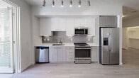 Located at 1105 E Katella Ave in Anaheim, California, this modern single-floor residence offers a clean, contemporary design with consistent light wood-tone flooring throughout. The open-concept layout connects the living area to the kitchen seamlessly, creating a bright and functional flow.

The kitchen is well-appointed with a full suite of stainless steel appliances, including a refrigerator with ice maker, range, built-in microwave, and dishwasher. Sleek two-tone cabinetry — white uppers paired with wood-finish lowers — is complemented by a neutral tile backsplash, light countertops, and a gold-accented sink fixture. Track lighting overhead adds both task illumination and a modern aesthetic touch. A sliding glass door adjacent to the kitchen opens directly onto a private balcony, allowing natural light to fill the space.

The living area is generously sized, with crisp white walls, a textured ceiling, and a window with blinds that brings in additional natural light. The bedroom features a dedicated walk-in closet with built-in shelving, offering practical storage solutions. The bathroom includes a full tub and shower combination, tile flooring, a vanity with storage, and a clean, understated finish throughout. The unit's overall design emphasizes modern simplicity and functional living.