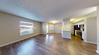 This single-floor residence offers a thoughtfully designed open-concept layout that seamlessly connects the living, dining, and kitchen areas. Rich wood-look flooring flows throughout the main living spaces, complemented by warm neutral-toned walls and textured ceilings that lend a cozy yet polished ambiance. Multiple windows fitted with blinds allow natural light to fill the space generously.

The kitchen is a standout feature, boasting white cabinetry, light quartz-style countertops, a double-basin sink, and a full suite of stainless steel appliances including a refrigerator, electric range, and microwave. A peninsula counter connects the kitchen to the living area, making it ideal for both cooking and entertaining. A pantry closet provides additional storage within the kitchen corridor.

The bedrooms are carpeted for comfort and each features windows that bring in natural light, ceiling fans, and closet access — one bedroom includes a walk-in closet. The bathroom is clean and functional, featuring a single vanity with ample counter space, under-sink cabinetry, a shower-tub combination, and wood-look flooring that ties back to the main living areas. Built-in linen storage adds practical convenience. Overall, the space presents a clean, move-in-ready interior with consistent finishes throughout.