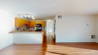 This single-floor residence offers a thoughtfully designed layout that balances functionality and comfort throughout. The open-concept kitchen is a standout feature, showcasing warm honey-toned wood cabinetry, granite countertops, and a matching granite tile backsplash that extends across the entire cooking area. Stainless steel appliances, including a refrigerator and range, complement the modern aesthetic, while a peninsula with a breakfast bar creates a seamless transition into the living area. Track lighting overhead ensures the kitchen is well-illuminated. Rich hardwood flooring extends through the main living and entry areas, lending warmth and cohesion to the open floor plan. The living space is generously proportioned, with clean white walls and a bright entry foyer featuring dual doors for added convenience. The bedrooms are carpeted for comfort and filled with natural light through large windows fitted with blinds. Each bedroom offers dedicated closet space, including a walk-in closet and a double sliding-door closet in separate rooms. The bathroom features tile flooring, a wood vanity with granite countertop, and a soaking tub with a shower. Throughout the unit, the neutral color palette and clean finishes create a bright, move-in-ready atmosphere.