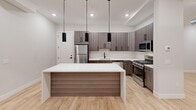 Located at 18 Lane Ave in Caldwell, NJ, this thoughtfully designed single-floor unit offers a seamless blend of modern aesthetics and functional living. Light-toned hardwood flooring flows consistently throughout the space, lending warmth and continuity to every room.

The open-concept kitchen serves as a centerpiece, featuring sleek wood-grain cabinetry, a large white quartz island with waterfall edge, stainless steel appliances, and striking black pendant lights that add a contemporary accent. Recessed lighting further enhances the bright, airy atmosphere.

The generously sized living area is defined by an exposed ductwork detail that adds an industrial-chic character, complemented by a row of windows dressed with natural-toned shades that invite ample natural light. Multiple additional rooms offer flexible use, each with clean white walls, recessed lighting, and windows with exterior views.

Two full bathrooms are finished to a high standard, featuring dark slate-style tile flooring, white vanities with matte black hardware, and glass-enclosed showers — one with a sliding barn-style door and walk-in shower, and another with a shower-tub combination. The consistent use of matte black fixtures throughout ties the design language together cohesively, creating a polished, modern living environment.