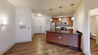 Located in the vibrant Dilworth neighborhood of Charlotte, NC, The Latta at Lexington Dilworth is a well-appointed one-bedroom, one-bathroom residence that combines modern design with functional living. The open-concept layout flows seamlessly from the kitchen into the living area, creating a welcoming and spacious feel throughout.

The kitchen is a standout feature, showcasing warm honey-toned cabinetry, dark granite countertops with a subtle tile backsplash, and a full suite of stainless steel appliances including a refrigerator, electric range, microwave, and dishwasher. A peninsula with pendant lighting overhead provides additional counter space and adds a refined, contemporary touch. Wood-style flooring runs throughout the main living areas, complementing the clean, neutral walls.

The bedroom offers a comfortable retreat, finished with plush carpeting, a ceiling fan, and a window with blinds that invites natural light while maintaining privacy. A dedicated closet provides convenient storage.

The bathroom is neatly designed with warm wood cabinetry, a granite-topped vanity, a framed mirror, and a full tub-shower combination with classic white tile surround. Consistent warm-toned wood flooring ties the bathroom to the overall aesthetic of the home. The layout is efficient and thoughtfully arranged, making excellent use of every square foot.
