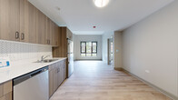 Located in Chicago's vibrant South Side neighborhood, this one-bedroom, one-bathroom unit at 1325 South Washtenaw Avenue offers a thoughtfully designed modern layout with efficient use of space. Light-toned hardwood-style flooring runs throughout, tying together each room with a clean, cohesive aesthetic.

The kitchen is well-appointed with warm wood-grain cabinetry extending from floor to ceiling, a crisp white countertop, and a herringbone-patterned tile backsplash. Stainless steel appliances — including a refrigerator, gas range, dishwasher, and microwave — complete the functional setup. The kitchen flows seamlessly into the open living area, which is brightened by large black-framed windows overlooking the surrounding neighborhood streetscape.

The bedroom is a quiet, comfortable retreat with its own large window that frames outdoor views of mature trees and neighboring architecture, allowing natural light to fill the room. A dedicated closet with wire shelving and hanging rods provides ample organized storage.

The bathroom features a full tub and shower combination with white subway tile surround, clean fixtures, and a straightforward, modern finish. The overall design of the unit is contemporary and neutral, making it a versatile and welcoming space in the heart of Chicago.