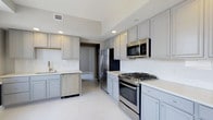 Located at 50 W Broad St in the heart of downtown Columbus, Ohio, this single-floor space offers a thoughtfully designed interior with contemporary finishes throughout. The kitchen serves as a central highlight, showcasing gray shaker-style cabinetry that extends to the ceiling, providing generous storage capacity. Crisp white countertops contrast elegantly with the cabinetry, creating a clean, modern aesthetic. Stainless steel appliances, including a gas range, built-in microwave, French door refrigerator, and dishwasher, outfit the kitchen with full functionality. A gold-toned faucet at the sink adds a refined accent detail. Recessed lighting illuminates the space evenly, complementing the light-toned tile flooring that runs throughout. The layout offers an efficient, galley-style flow, with ample counter space on both sides for meal preparation. A doorway visible from the kitchen suggests a well-connected floor plan, allowing for easy movement throughout the space. The overall design balances practicality with modern style, making it well-suited for everyday living in a prime urban location.