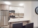Located at 49 Walnut St, Unit 2312, in Hamilton, Ontario, this modern 1-bedroom, 1-bathroom condominium offers 520 square feet of thoughtfully designed living space on a single floor. The open-concept layout connects the living area to the kitchen, creating an efficient and functional flow throughout the unit.

The living room is bright and airy, featuring large floor-to-ceiling sliding glass doors that frame expansive city views and flood the space with natural light. Light-toned laminate flooring runs consistently throughout, complementing the crisp white walls and contemporary aesthetic. The kitchen is fitted with modern cabinetry in a warm wood-tone finish, stainless steel appliances including a refrigerator and dishwasher, and a central island that provides additional counter space.

The bedroom measures 100 square feet and includes large windows offering elevated urban views, enhancing the sense of openness in the compact space. The bathroom features a wood-framed vanity mirror, a quartz or stone-topped vanity with an undermount sink, and clean, neutral finishes that reflect a modern design sensibility.

A hallway connects the key spaces of the unit, contributing to a logical and practical layout. The consistent use of light materials and large windows throughout the unit creates a cohesive, bright atmosphere well-suited for urban living in downtown Hamilton.