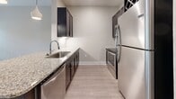 Located at 13504 Citicards Way in Jacksonville, FL 32258, this efficiently designed 580-square-foot, one-bedroom, one-bathroom apartment offers a well-planned single-floor layout. The open-concept living and kitchen area features light hardwood-style flooring, recessed and pendant lighting, and a granite-topped breakfast bar peninsula that seamlessly connects the two spaces. The kitchen is outfitted with dark espresso cabinetry, granite countertops, a tile backsplash, stainless steel appliances including a refrigerator, dishwasher, microwave, and range, plus a built-in wine rack above the cabinetry. The 160-square-foot primary bedroom is carpeted and includes a ceiling fan, natural light from dual windows with exterior views, and direct access to a dedicated closet. The bathroom features hardwood-style flooring, a dark vanity with granite countertop and framed mirror, a full soaking tub with marble-style tile surround, and direct access from the bedroom. Neutral wall tones and clean white trim throughout create a cohesive, modern aesthetic across the entire unit.