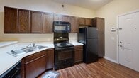 Located at 617 N Notre Dame Ave in South Bend, Indiana, this single-story, one-bedroom, one-bathroom residence offers a thoughtfully designed layout that maximizes its compact footprint. The open-concept kitchen serves as a focal point of the living area, featuring rich dark-stained wood cabinetry, a full suite of black appliances including an electric range, built-in microwave, dishwasher, and refrigerator, as well as light-toned countertops and a double-basin sink. A peninsula counter separates the kitchen from the living area, creating a natural flow between spaces. The kitchen and main living areas are finished with warm hardwood-style flooring, adding a cohesive and polished look throughout. The bedroom is carpeted and generously proportioned, offering a large window that invites natural light and views of the surrounding greenery. Adjacent to the bedroom is a full bathroom with wood-toned vanity cabinetry and hardwood-style flooring, which opens directly into a dedicated walk-in closet equipped with multiple hanging rods and shelving — providing ample storage. The neutral, warm beige color palette throughout the space creates a bright and welcoming ambiance, well-suited for comfortable everyday living.