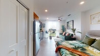 Located at 1200 NW Tenth Ave in Miami's Health District, this thoughtfully designed studio offers a seamless open-plan layout that integrates the sleeping, living, and dining areas into one cohesive space. Large windows with sheer white curtains flood the interior with natural light, while a ceiling fan adds a breezy, tropical feel that complements the lush botanical décor throughout.

The kitchen is a functional highlight, featuring warm walnut-toned cabinetry with gold hardware, white quartz countertops, a subway tile backsplash, and a full suite of stainless steel appliances including a refrigerator, electric range, microwave, and dishwasher. A compact dining area with bar-height seating sits just adjacent, making efficient use of the space.

The main living area comfortably accommodates a full bed and a sofa seating area, anchored by a patterned area rug and nature-inspired artwork. The entryway corridor includes louvered closet doors for storage, with a full-length mirror enhancing the sense of depth.

The bathroom is finished with warm tile flooring, a walnut vanity with a white countertop, a glass-enclosed walk-in shower, and coordinated gold-toned shelving accents. The overall aesthetic is clean, modern, and Miami-inspired, offering a polished and livable retreat in the heart of the city.