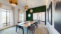 Located at 4535 SW 54th St Rd in Ocala, Florida, this thoughtfully designed collaborative workspace comprises two distinct yet connected rooms, offering a refined environment for meetings, brainstorming sessions, or private gatherings. The space makes a striking first impression with a full-height living green wall that serves as a natural divider between the two rooms, adding vibrant texture and an organic warmth to the interior. Pendant lighting with woven rattan shades hangs from the elevated ceilings, casting a warm, ambient glow throughout. The primary room features a large wood-top conference table surrounded by contemporary upholstered chairs, all set atop patterned multi-tone carpeting. Floor-to-ceiling windows dressed with sheer linen drapes flood the room with natural light and offer views of the surrounding landscape. A bold abstract mountain mural anchors one wall, adding dramatic artistic depth. The adjoining room continues the design narrative with an eye-catching undulating line-pattern wall adorned with framed equestrian artwork, alongside another wood conference table and a sleek geometric ring chandelier. Together, the two rooms create a cohesive, design-forward environment that balances creativity and functionality.