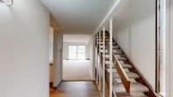 This two-floor residence offers a practical and well-appointed layout designed for comfortable everyday living. The entry level welcomes you with hardwood-style flooring and a staircase featuring a classic wooden handrail with white balusters, leading to the upper floor. Adjacent to the entry, the carpeted living room is a generous, light-filled space anchored by a white-painted brick accent wall and a sliding glass door that opens to a private balcony, filling the room with natural light and offering outdoor views. Baseboard heating is present throughout the home for efficient climate control.

The kitchen is efficiently designed with gray upper cabinetry, white lower cabinetry, granite-style countertops, a double stainless steel sink, and black appliances including a range and dishwasher. The dedicated laundry room houses a full-size washer and dryer alongside overhead cabinetry for added storage convenience.

The bedrooms feature plush carpeting and expansive louvered bi-fold closet doors offering exceptional storage capacity. One bedroom benefits from direct sliding door access to a balcony. The bathroom is clean and functional, complete with a tub-shower combination, wood-look flooring, and brushed nickel fixtures. Overall, the space presents a neutral, move-in-ready aesthetic throughout.