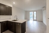 Located at 1547 Pacific Avenue in Santa Cruz, California, this modern one-bedroom, one-bathroom residence offers a thoughtfully designed open-concept layout with clean lines and contemporary finishes throughout. Light wood-tone flooring flows seamlessly across the entire unit, complementing the bright white walls and recessed lighting that give the space an airy, well-lit feel.

The kitchen is a standout feature, showcasing rich dark wood cabinetry, striking quartz countertops with elegant veining, and a full suite of stainless steel appliances including a refrigerator, range, microwave, and dishwasher. A peninsula with an undermount sink doubles as a casual dining or prep space, opening directly into the living area for effortless flow.

The living area is generously proportioned, offering access to a private balcony through a sliding glass door that frames views of the surrounding Santa Cruz neighborhood, filling the space with natural light. The bedroom is a comfortable retreat with a large window providing additional outdoor views and ample natural illumination. A spacious walk-in closet with built-in shelving and hanging rods provides excellent storage. The bathroom features a full soaking tub with shower, a dark wood vanity with white quartz countertop, and a large mirror, all finished with the same modern aesthetic found throughout the residence.