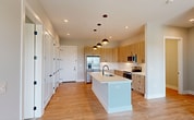 This 1,100 sq ft single-floor apartment in Wilmington, NC offers a thoughtfully designed layout with 2 bedrooms, 2 bathrooms, and 2 closets. The open-concept kitchen and living area serves as the heart of the home, featuring light wood cabinetry, quartz countertops, a center island with an undermount sink and matte black faucet, stainless steel appliances, and stylish pendant lighting — all complemented by light hardwood-style flooring throughout. The living area flows seamlessly from the kitchen, providing an airy, connected feel. The primary bedroom spans 190 sq ft and is finished with plush carpet and neutral tones. Both bedrooms are served by well-appointed walk-in closets with built-in shelving and dual hanging rods for ample storage. The bathrooms feature light wood vanities with black-framed mirrors and modern fixtures, maintaining a consistent contemporary aesthetic. A standout feature is the private balcony, offering elevated views of a serene pond, landscaped courtyard with a covered pavilion, and open wetland — filling the unit with natural light and a sense of openness. The unit's soft neutral palette, clean lines, and modern hardware create a cohesive and inviting living environment throughout.