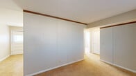 This single-floor unit offers a straightforward, functional layout designed for comfortable everyday living. The entryway opens into a carpeted living area bathed in neutral tones, with clean white walls and easy access to the adjoining kitchen. The kitchen is well-equipped with white cabinetry spanning both upper and lower sections, providing ample storage. It features a full suite of appliances including a refrigerator, electric range, built-in microwave, and dishwasher, all complemented by a double-basin sink. Light tile flooring in the kitchen adds a practical, easy-to-maintain surface. The bedrooms are carpeted and finished in soft, neutral tones, each benefiting from multiple windows fitted with blinds that allow for adjustable natural light. One bedroom features a large sliding-door closet that spans nearly the full width of the wall, offering generous storage capacity. Throughout the unit, consistent use of beige carpet, white trim, and warm neutral wall colors creates a cohesive and understated aesthetic. The space is clean, move-in ready, and well-suited for those seeking a straightforward, low-maintenance living environment with practical features and adequate natural light.