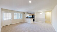 This single-floor, 2-bedroom, 1-bathroom residence features a practical and well-organized layout designed for comfortable living. The open-plan living and kitchen area forms the heart of the home, where soft, neutral-toned carpet flows throughout the living space and a ceiling fan provides overhead comfort. A large window fitted with vertical blinds fills the room with natural light and contributes to an airy atmosphere. The kitchen is efficiently designed with light maple cabinetry, dark granite-style countertops, and black appliances including a gas range and a full-size refrigerator. A peninsula counter with a matching countertop serves as a natural divider between the kitchen and living area, offering additional prep or casual dining space. Built-in open shelving in the kitchen adds convenient storage. The spacious primary bedroom features recessed lighting and plush carpet, providing a generous and restful retreat. The second bedroom is well-proportioned with carpet flooring and a window offering natural light. Both rooms share access to a full bathroom appointed with full-height stone-look tile surrounding a soaking tub and shower combination. A dedicated closet rounds out the unit's practical storage options. The overall aesthetic is clean, neutral, and move-in ready.