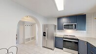 Located at 1122 Wellman Ave NE in Huntsville, Alabama, this single-story, 2-bedroom, 1-bathroom home offers a well-designed layout with thoughtful updates throughout. The kitchen serves as a standout feature, showcasing navy blue shaker-style cabinetry with gold hardware, granite-look countertops, stainless steel appliances including a French door refrigerator, electric range, and built-in microwave, all set atop gleaming marble-look porcelain tile floors. Shiplap wall accents and a natural wood floating shelf add rustic-modern character. The living room is bright and welcoming, featuring hardwood flooring, large windows with outdoor views of lush greenery, and clean white walls that keep the space feeling open. The primary bedroom is a comfortable retreat with a large picture window overlooking the yard, hardwood floors, and a pendant light fixture. The second bedroom, also with hardwood flooring, offers flexibility as a home office or guest room. The bathroom is cleanly updated with marble-look tile surrounding the tub and shower, a black-framed window, and open shelving. A dedicated utility room houses a stacked washer and dryer unit alongside additional cabinetry and a dishwasher, maximizing functionality. A sliding barn door accent adds a stylish touch to the interior hallways.