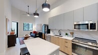 Located in Doral, FL, this thoughtfully designed one-bedroom, one-bathroom residence offers a contemporary open-concept layout that maximizes every inch of its well-proportioned floor plan. Soaring ceilings throughout create an airy, expansive atmosphere, while light-toned flooring unifies the living spaces seamlessly.

The kitchen is a standout feature, boasting a two-tone cabinetry scheme pairing matte gray upper cabinets with warm wood-finish lower cabinets, a striking marble-look tile backsplash, white quartz countertops, and a full suite of stainless steel appliances. A central island with bar seating provides additional workspace and casual dining. Stylish pendant lighting adds a modern accent overhead. An in-unit stacked washer and dryer add everyday convenience.

The living room benefits from a large window framing lush outdoor greenery, filling the space with natural light. High ceilings amplify the sense of openness in this intimate yet comfortable area.

The bedroom is a serene retreat with soaring ceilings, a window for natural light, and direct access to the bathroom. The bathroom features large-format neutral tiles, a glass-enclosed walk-in shower with a rainfall fixture, open wood shelving for storage, and a clean, minimalist vanity. A dedicated closet completes this well-appointed residence.