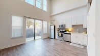 Located at 144 Moreland Ave NE in Atlanta's vibrant Inman Park neighborhood, this single-floor unit offers an efficiently designed layout that maximizes every square foot. The open-plan kitchen and living area is immediately striking for its dramatically tall ceilings, which create a strong sense of volume and airiness well beyond what the footprint might suggest. Large clerestory windows and a sliding glass door flood the space with natural light and provide direct access to an outdoor patio framed by a stone accent wall.

The kitchen is outfitted with stainless steel appliances—including a refrigerator, electric range, over-the-range microwave, and dishwasher—complemented by white shaker-style cabinetry, a gray subway tile backsplash, and light countertops. A built-in open shelving unit adds functional display space. Light-toned hardwood-style flooring runs throughout, enhancing the clean, contemporary aesthetic.

A narrow hallway connects the main living area to the rest of the unit, featuring a louvered storage closet and high transom windows that continue the theme of elevated ceilings. The bathroom is finished with large-format earth-toned tiles surrounding a full soaking tub and shower combination, paired with neutral walls for a grounded, spa-like feel.