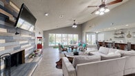Located along US Highway 277 in Abilene, Texas, this single-story clubhouse offers a well-appointed, open-concept layout with a warm rustic-modern aesthetic throughout. The entrance leads directly into the main living area, where vaulted ceilings and light wood-style flooring create an airy, welcoming atmosphere. The focal point of the living room is a striking floor-to-ceiling reclaimed wood accent wall, which frames a fireplace and wall-mounted television, adding texture and character to the space. Dual ceiling fans enhance comfort throughout. Large picture windows line one wall of the living area, flooding the space with natural light and offering direct views of the outdoor pool and landscaped surroundings. An indoor putting green tucked beneath the windows adds a fun, recreational touch. The kitchen features dark cabinetry with quartz countertops, open industrial-style shelving, stainless steel appliances, and a rustic corrugated metal island with bar seating — a standout design detail that ties the space's farmhouse-inspired character together. Throughout, neutral gray walls, cowhide accents, and carefully chosen furnishings reinforce the cohesive rustic-modern theme, making this clubhouse a versatile and inviting gathering space.