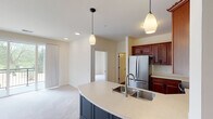 This single-floor residence offers a well-designed layout that balances functionality and comfort throughout its living spaces. The kitchen serves as a central highlight, featuring rich cherry wood cabinetry, stainless steel appliances including a refrigerator, range, and built-in microwave, and a curved island with a double undermount sink and light countertops. Pendant lighting above the island adds a refined touch, while durable hardwood-style flooring completes the space.

The open living area flows directly from the kitchen and is finished with plush carpeting. Large windows and a sliding glass door provide abundant natural light and direct access to a private balcony overlooking green outdoor surroundings.

The bedrooms are carpeted and bright, each featuring sizable windows—some with scenic outdoor views. One bedroom includes access to a dedicated walk-in closet with built-in shelving and rod systems. 

Two bathrooms serve the residence. The primary bathroom features a double-sink vanity with rich wood cabinetry and a wide mirror, while the secondary bathroom includes a single vanity and a full tub-shower combination. A dedicated laundry area houses a full-size washer and dryer with overhead cabinetry for additional storage.
