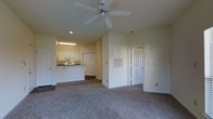 This single-floor residence offers a comfortable and functional layout with a welcoming open-concept design. The main living area is finished with plush wall-to-wall carpeting, creating a warm and cozy atmosphere. A ceiling fan is centrally mounted overhead, providing both ventilation and a subtle decorative touch to the space.

The kitchen is situated adjacent to the living area and is defined by white cabinetry that extends to the upper walls, offering ample storage. A built-in microwave and a dark countertop peninsula add practicality, while under-cabinet lighting illuminates the workspace. The kitchen flows naturally into the main living space, making it well-suited for everyday living and entertaining.

The layout also features multiple doorways leading to additional rooms, suggesting a thoughtful floor plan with distinct private and shared zones. Panel-style doors with classic detailing contribute to the clean, traditional aesthetic carried throughout the unit. Neutral wall tones in soft white and cream keep the interior feeling bright and airy, while recessed lighting supplements the overall illumination. The space strikes a balance between practicality and comfort, making it a versatile residential setting.