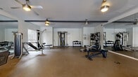 This fitness center in Hoover, Alabama offers a spacious, single-floor layout designed to accommodate a comprehensive range of workout activities. The open floor plan is covered in durable rubber flooring, providing a safe and functional surface for exercise throughout the space.

The cardio section is well-appointed with multiple treadmills, elliptical trainers, a stationary bike, and a rowing machine, all positioned near large windows that invite natural light and offer outdoor views. Ceiling fans are distributed throughout the space, ensuring comfortable air circulation during workouts.

The strength training area features a cable crossover machine, a lat pulldown/cable station, adjustable benches, and a dumbbell rack stocked with free weights. Additional selectorized machines round out the resistance training options, providing equipment for a full-body workout routine.

Large wall-to-wall mirrors line sections of the room, visually expanding the space and allowing users to monitor their form during exercise. Exposed dark ceiling beams add a distinctive architectural contrast against the white walls and ceiling. Multiple windows on several walls flood the interior with natural light, contributing to an open and energizing atmosphere. The overall environment is clean, well-maintained, and thoughtfully organized for an efficient fitness experience.