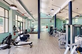 Located at 2151 Cumberland Pkwy SE in Atlanta, GA, this well-appointed fitness center offers a spacious, single-floor layout designed to accommodate a comprehensive range of workout activities. The facility is characterized by soaring vaulted and high ceilings that lend an open, airy atmosphere throughout the space.

Large floor-to-ceiling windows line the walls, flooding the interior with natural light and offering views of the surrounding greenery. The soft mint-green walls, paired with bold navy structural columns and light wood-style flooring, create a clean and energizing aesthetic.

The main workout floor is generously proportioned and houses a robust selection of Matrix-brand strength training machines, including cable systems, leg press equipment, and multi-functional units. A dedicated cardio zone features a row of Matrix treadmills, upright and recumbent bikes, rowing machines, and stair climbers. Floor-to-ceiling mirrors span much of the perimeter, enhancing the sense of space and supporting form monitoring during exercise.

A glass-partitioned studio area provides an ideal setting for functional training, stretching, or group exercise, and is stocked with stability balls, kettlebells, and other accessories. Industrial-style exposed ductwork and pendant lighting add a modern edge, while ceiling fans maintain comfortable airflow. Double-door access at the rear connects directly to an outdoor area, further extending the facility's usability.