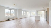 Located at 22 Hubbard Road in Wilton, CT, this contemporary two-story residence offers a bright, minimalist aesthetic defined by clean lines, white walls, and light hardwood flooring throughout. The main floor is generously proportioned, anchored by an expansive open-concept living and kitchen area filled with natural light from a series of large windows overlooking the surrounding landscape. The modern kitchen features a substantial white island with an integrated sink, sleek flat-front cabinetry, stainless steel appliances including a French door refrigerator, microwave, and range, plus track lighting overhead. The living area flows seamlessly from the kitchen, creating an airy, versatile space ideal for both everyday living and entertaining. The upper floor houses the primary bedroom, a well-sized room with wide windows framing outdoor views of the Wilton neighborhood. A door leads to an exterior balcony area, extending the sense of openness. Two closets provide practical storage, including a walk-in closet fitted with wire shelving. All three bathrooms are finished with large-format neutral stone-look tiles, soaking tubs with overhead rain showers, and light tile flooring, delivering a calm, spa-like atmosphere. The overall design emphasizes simplicity, natural light, and functional flow throughout both levels.