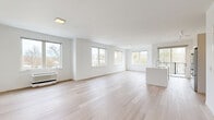 Located at 22 Hubbard Road in Wilton, CT, this contemporary two-story residence offers a bright, minimalist aesthetic defined by clean lines, white walls, and light hardwood flooring throughout. The main floor is generously proportioned, anchored by an expansive open-concept living and kitchen area filled with natural light from a series of large windows overlooking the surrounding landscape. The modern kitchen features a substantial white island with an integrated sink, sleek flat-front cabinetry, stainless steel appliances including a French door refrigerator, microwave, and range, plus track lighting overhead. The living area flows seamlessly from the kitchen, creating an airy, versatile space ideal for both everyday living and entertaining. The upper floor houses the primary bedroom, a well-sized room with wide windows framing outdoor views of the Wilton neighborhood. A door leads to an exterior balcony area, extending the sense of openness. Two closets provide practical storage, including a walk-in closet fitted with wire shelving. All three bathrooms are finished with large-format neutral stone-look tiles, soaking tubs with overhead rain showers, and light tile flooring, delivering a calm, spa-like atmosphere. The overall design emphasizes simplicity, natural light, and functional flow throughout both levels.