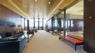 Located at 777-799 Main St in Hartford, Connecticut, this distinguished high-rise office space offers an exceptional blend of classic architectural design and modern functionality. Floor-to-ceiling windows throughout flood the interiors with natural light while framing sweeping panoramic views of the Hartford skyline and surrounding landscape.

The main corridor serves as an elegant spine, featuring a warm gold ceiling with recessed lighting, neutral carpeting, and glass-walled conference or office areas that maintain an open, transparent feel. Private offices are appointed with rich wood-paneled walls, deep blue lacquered ceilings, built-in wood desks with gold-tone surfaces, and direct access to outdoor terrace areas overlooking the city.

A formal reception or gallery area showcases polished marble tile flooring, floor-to-wall dark wood paneling, and curated framed artwork, lending a refined, professional ambiance. The fitness area is accessed through a marble-floored foyer with premium wood and stone wall finishes, opening to well-equipped workout rooms.

Social and lounge areas offer distinct personalities — one features a bold yellow sectional sofa with contemporary art, while another presents warm rose-toned seating against wood-paneled walls beneath a rich burgundy ceiling. A casual dining area with bentwood chairs and light wood tables completes the space, all oriented toward the expansive exterior views.