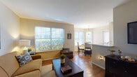 This single-floor residence offers a thoughtfully designed open layout that connects the living, dining, and kitchen areas into a cohesive and functional living space. The living room is bright and welcoming, featuring hardwood-style flooring, neutral warm-toned walls, and a large window that fills the space with natural light and offers views of surrounding greenery. A front entry door opens directly into this comfortable area, creating an easy flow throughout the unit.

The dining area is positioned adjacent to the living room and benefits from its own set of windows, allowing ample natural light. A pendant light fixture overhead adds a refined touch to the space. The galley-style kitchen is efficiently laid out with warm wood cabinetry, white appliances, light countertops, and a convenient pass-through to the dining and living areas. A notable feature is the in-unit laundry area tucked at the end of the kitchen corridor.

The primary bedroom is generously sized with plush carpeting and a sliding glass door that opens to an outdoor space, providing both natural light and fresh air. The second bedroom also features carpeted flooring and a ceiling fan. Both bathrooms are clean and functional, each featuring a tub-shower combination with white tile surround and hardwood-style flooring.