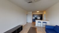 Located at 503 George Bush Dr W in College Station, Texas, this single-floor unit offers a practical and well-designed layout suited for everyday living. The open-concept living area is finished with light wood-style flooring and features a ceiling fan, providing a bright and airy atmosphere. A large window allows natural light to fill the space, offering a view to the exterior. The kitchen is equipped with dark espresso cabinetry, black appliances including a refrigerator, electric range, and microwave, as well as a sink and ample counter space. A breakfast bar with seating connects the kitchen seamlessly to the living area, making it ideal for casual dining and entertaining. Both bedrooms are carpeted and include ceiling fans and windows with blinds that allow for natural light and privacy. Each room offers enough space to accommodate a bed, desk, and additional storage furniture. The bathroom is clean and functional, featuring a dark wood vanity with a white countertop, a large mirror, and a full tub-shower combination with tile surround and wood-style flooring. Throughout the unit, the neutral color palette and consistent finishes contribute to a cohesive and modern aesthetic.