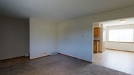 Located at 5368 Big Tyler Rd in Cross Lanes, West Virginia, this two-floor property presents a straightforward and functional layout designed for comfortable everyday living. The main living area features wall-to-wall carpeting in a neutral tone, creating a warm and understated foundation that adapts easily to a variety of furnishing styles. Light-colored walls throughout contribute to a clean, open atmosphere, while a floor-level ventilation register indicates a forced-air heating and cooling system for year-round climate control. A thermostat is visibly mounted on the wall, offering convenient access to temperature management. The living space flows directly into the kitchen, which is visible through a connecting doorway. The kitchen features warm honey-toned wood cabinetry, dark countertops, and tile-style flooring that contrasts with the carpeted living area, providing a practical and easy-to-maintain surface. The open sightline between the two spaces supports a connected, cohesive feel. Spanning two floors, the property offers additional space above, suitable for bedrooms or other private living areas. The overall ambiance is clean, neutral, and move-in ready.