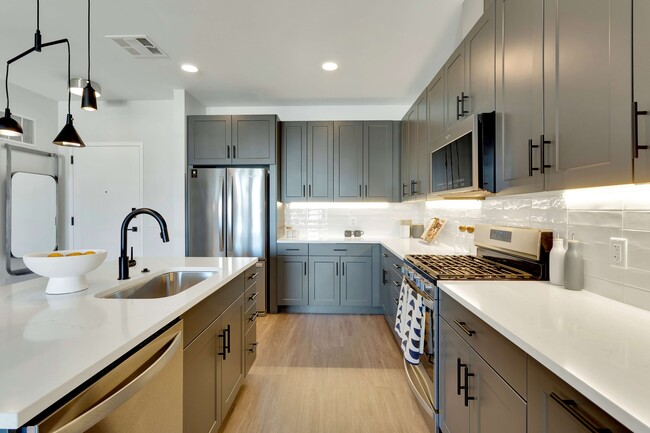Modern kitchen with sleek grey cabinets, stainless steel appliances, and elegant pendant lighting, offering a bright and inviting atmosphere. - The Fitzgerald