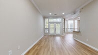 This single-floor residence offers a thoughtfully designed layout with a bright, open living area as its centerpiece. The main living space is finished with light hardwood flooring and features elegant crown molding, recessed lighting, and a set of French doors flanked by transom windows that invite an abundance of natural light and provide views of surrounding greenery. A bay window configuration extends the living area, enhancing the sense of openness.

The kitchen is outfitted with white cabinetry, granite countertops, a classic subway tile backsplash, and stainless steel appliances, including a range with overhead microwave. A breakfast bar connects the kitchen to an adjacent dining or flex area, which includes built-in shelving, a granite-topped built-in desk, and additional open shelving — offering both functional storage and display space.

The bedroom features plush carpeting, generous wall space, and a striking curved bay window that frames outdoor views. A walk-in closet with wire shelving systems provides ample storage. The bathroom includes a full soaking tub with a shower curtain rod, clean white tile surround, and light tile flooring, maintaining the home's neutral, cohesive aesthetic throughout.