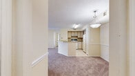 This single-story unit offers a practical and comfortable layout across three bedrooms and two full bathrooms. The open-concept living and kitchen area forms the heart of the home, where light-toned walls and warm carpet flooring create a welcoming atmosphere. The kitchen features a peninsula with a countertop overhang, light wood cabinetry, tile backsplash, tile flooring, and white appliances including an electric range and refrigerator. A pendant light fixture above the peninsula adds a subtle design touch.

The living area flows seamlessly from the kitchen and features a sliding glass door that opens to a private balcony, providing natural light and outdoor views of the surrounding greenery and neighboring buildings. A ceiling fan with a light fixture overhead adds comfort to the space.

Each of the three bedrooms is carpeted and finished with the same warm, neutral tones. Two bedrooms feature ceiling fans and windows with slatted blinds that bring in natural light and views of lush trees outside. The primary bedroom is a comfortable size and shares the same design consistency.

Both bathrooms are finished with light tile flooring and include full tub-shower combinations with white tile surrounds and chrome fixtures, providing clean and functional spaces. A hallway connects all rooms, completing the efficient and cohesive floor plan.