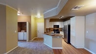 This single-floor residence offers a thoughtfully designed open-concept layout that seamlessly connects the living area to the kitchen. The living space features plush carpeting and warm neutral-toned walls accented by crisp white crown molding, creating an inviting atmosphere. The kitchen is well-equipped, boasting white cabinetry, granite-style countertops, hardwood-style flooring, and a full suite of black appliances including a gas range, built-in microwave, dishwasher, and a stainless steel refrigerator. A peninsula with a double sink serves as both a functional workspace and a natural divider between the kitchen and living areas. A dedicated laundry area with a washer and dryer is conveniently accessible. The bedrooms are generously sized, each featuring plush carpeting, warm wall tones, and ample natural light through blinds-fitted windows. Closet space is provided in the bedrooms, offering practical storage solutions. The bathrooms are finished with granite-style countertops, white cabinetry, large vanity mirrors, and a tub-shower combination with clean white tile surround. Hardwood-style flooring continues through the bathrooms, tying the design together cohesively throughout this comfortable, move-in ready home.