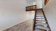 This two-story space is defined by a well-designed interior that balances functional layout with clean, modern finishes throughout both levels. The lower level showcases wood-look plank flooring that extends across an open living area, anchored by a prominent staircase fitted with carpet treads and a rich, warm-toned wood railing with vertical slatted detailing. The upper-level landing overlooks the lower floor through a matching wood balustrade, adding visual depth and an open, airy quality to the space.

The upper level features multiple carpeted rooms finished in neutral tones, offering a comfortable and quiet feel. One room includes a window with natural light and a baseboard heater, while another provides a closet with bifold doors. Additional carpeted rooms on this level are spacious and versatile.

The kitchen on the lower level is well-appointed with white shaker-style cabinetry, gray countertops, stainless steel appliances including a range and refrigerator, and a classic white subway tile backsplash over wood-look flooring. The bathroom is cleanly finished in all-white with a tub-shower combination, a vanity, and wood-look flooring. Throughout, the space maintains a bright, neutral palette.