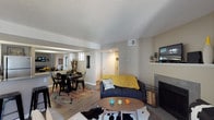 This single-story residence is thoughtfully laid out to maximize functionality and flow throughout its living spaces. The open-concept living and dining area serves as the heart of the home, anchored by a tiled fireplace and hardwood-style flooring. A sliding glass door in the living room provides direct access to a private outdoor patio, filling the space with natural light and outdoor views. The textured ceilings and neutral warm-gray walls create a cohesive backdrop throughout.

The kitchen is well-appointed with white cabinetry, stainless steel appliances including a refrigerator and range, and a granite-style countertop peninsula offering bar seating for casual dining. It opens directly to the dining area, reinforcing the open layout.

The primary bedroom is carpeted and generously sized, featuring a window for natural light and direct access to an en-suite bathroom equipped with a white vanity, granite-style countertop, and a tub-shower combination. A second flexible room with carpet, a large window, and open shelving units serves well as a den or office. A second full bathroom with a single-sink vanity and tub-shower completes the layout.