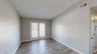 Located at 4250 Branch Bend Ln in Charlotte, NC, this single-story, three-bedroom, two-bathroom home offers a practical and comfortable layout. The living room is bright and open, featuring wood-look laminate flooring, neutral gray walls, a textured ceiling, and a set of white French doors that let in natural light and provide outdoor access. The kitchen is well-appointed with white cabinetry, light countertops, a stainless steel sink, a dishwasher, and black appliances including a range and refrigerator. A peninsula-style counter connects the kitchen to the living area, creating an open flow between the two spaces. The three bedrooms are carpeted for warmth and comfort, each featuring neutral tones and natural light from windows. The primary bedroom is generously sized and includes a ceiling fan with light fixture. Both bathrooms are finished with wood-look flooring, white vanity cabinets, light countertops, framed mirrors, and dark-finish faucets. One bathroom features a full tub-shower combo with tile surround. Additional spaces include a hallway, a closet, and a utility room. The home's clean, neutral palette throughout offers a move-in ready feel.