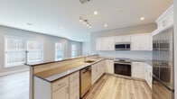 Located at 57 W Merritt Blvd in Fishkill, NY, this thoughtfully designed single-floor residence offers a clean, modern aesthetic with consistent finishes throughout. Light wood-tone flooring flows seamlessly across the living areas and bedrooms, complemented by neutral warm and cool gray wall tones that create a bright, welcoming atmosphere.

The kitchen is a standout feature, showcasing white shaker-style cabinetry, dark quartz countertops, a white subway tile backsplash, and a full suite of stainless steel appliances including a range, over-the-range microwave, dishwasher, and refrigerator. A peninsula with an overhang provides additional seating and defines the open-concept layout, while track lighting and recessed fixtures ensure well-lit workspaces. Multiple windows allow natural light to fill the kitchen and living areas.

The bedrooms are generously proportioned with ample natural light from large windows and light-toned flooring. The bathroom is finished with marble-look tile flooring, a soaking tub with a subway-tiled surround, and a gray vanity with a white countertop. A dedicated laundry room houses a full-size Samsung washer and dryer with overhead shelving. A clean hallway with gray modern doors connects the living spaces, completing this well-appointed, move-in-ready residence.