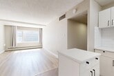 Located in downtown Edmonton at 103 Avenue NW, this 2-bedroom, 1-bathroom unit offers a practical and well-appointed layout across a single floor. Light-toned hardwood flooring runs throughout the main living areas and bedrooms, lending a clean and cohesive look to the space.

The living room is a bright, open area featuring a large window dressed with neutral curtains that allow generous natural light to fill the room. A peninsula-style countertop separates the living area from the kitchen, which is equipped with white cabinetry, upper storage, and a white stove, providing a functional workspace within a compact footprint. A closet near the entry offers convenient storage.

Both bedrooms are finished with the same light hardwood flooring and feature windows that bring in natural light. The primary bedroom includes a mirrored sliding closet, maximizing the sense of space, while the second bedroom also offers closet storage. Neutral taupe wall tones throughout the unit create a calm and versatile backdrop.

The bathroom is finished with rich dark-brown wall and floor tiles, a white soaker tub, a white vanity with under-cabinet storage, and a mirror — offering a clean contrast to the lighter tones found elsewhere in the unit. A hallway connects the main rooms, completing the efficient and straightforward floor plan.