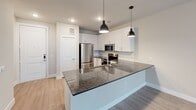 This single-story unit in Austin, TX offers a thoughtfully designed open-concept layout that seamlessly connects the kitchen, dining, and living areas. The kitchen serves as a central focal point, showcasing a large island with dark granite countertops, an undermount sink, and pendant lighting overhead. White shaker-style cabinetry lines the walls, complemented by a full suite of stainless steel appliances, including a refrigerator, range, microwave, and dishwasher. Light wood-style flooring flows throughout the main living areas, adding warmth and continuity to the space.

The living area is spacious and bright, featuring a ceiling fan, large windows, and a glass-paned door that invites natural light and outdoor views. The neutral wall tones throughout create a clean, versatile backdrop.

The bathroom is well-appointed with white cabinetry, granite countertops, tile flooring, and recessed lighting, offering a bright and functional layout. Adjacent to the bathroom, the bedroom includes a generously sized walk-in closet outfitted with multiple hanging rods and shelving, providing substantial storage. The overall design of the space is modern and move-in ready.
