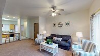This two-floor residence at 1111E offers a well-organized layout designed for comfortable, everyday living. The main-level living room is a welcoming space finished with plush carpeting, a ceiling fan with light fixture, and a large window that draws in natural light. The open sightlines connect the living area to the kitchen, which features warm honey-toned wood cabinetry, tile flooring, ample counter space, and a full suite of appliances including a refrigerator, electric range with over-the-range microwave, and a double sink. The main level also includes a bathroom with a wood-toned vanity, tile flooring, and a lighted mirror above the sink. The bedrooms are carpeted and quiet, each with windows providing natural light. One bedroom features a distinctive rustic barn-style headboard wall with flanking sconce lighting, adding a charming accent. A second bedroom offers a closet with sliding mirrored doors. The lower level provides an additional spacious carpeted room — ideal as a family room or recreation space — with recessed lighting and a utility door. A second full bathroom with a shower/tub combination completes the lower level. Throughout the home, neutral tones and consistent finishes create a cohesive, livable atmosphere.