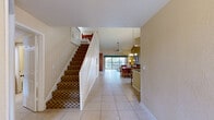 Located in Kissimmee, Florida, this two-story home offers a well-designed layout across three bedrooms and four bathrooms. The main floor impresses with soaring vaulted ceilings that amplify the sense of openness throughout the living and dining areas. The living room features large sliding glass doors that open to a private balcony with outdoor seating, allowing ample natural light to fill the space. A built-in wood entertainment center adds a functional focal point to the room. The dining area is anchored by an elegant chandelier and benefits from an arched window overhead, while the adjacent kitchen features rich dark wood cabinetry, granite countertops, stainless steel appliances, and a breakfast bar with seating. An open staircase with white railings leads to the upper level. The generously sized primary bedroom includes direct balcony access, vaulted ceilings, and a luxurious en-suite bathroom complete with a soaking jetted tub, a glass-enclosed shower, dual vanities with granite countertops, and tile flooring. Additional bedrooms are carpeted, feature vaulted ceilings and ceiling fans, and share well-appointed bathrooms. Light tile flooring flows throughout the main living areas, completing this bright and comfortable Florida retreat.