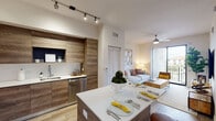 This well-appointed single-floor residence offers a thoughtfully designed open-concept layout that seamlessly connects the kitchen, dining, and living areas. The kitchen serves as a central highlight, featuring floor-to-ceiling wood-grain cabinetry, stainless steel appliances including a refrigerator, microwave, range, and dishwasher, and crisp white quartz-style countertops. A central kitchen island with matching countertop provides additional dining and prep space, complemented by bar stools for casual seating. Track lighting overhead ensures the area is well illuminated throughout.

The living area extends naturally from the kitchen, offering ample space for relaxation. Ceiling fans are present in both the living area and bedrooms, promoting comfortable airflow. Sliding glass doors in the living space invite natural light and provide access to an outdoor area.

The bedrooms are calm and comfortable, each featuring luxury vinyl plank flooring, natural light from well-placed windows with blinds and sheer curtains, and ceiling fans. The primary bedroom includes an en-suite bathroom access, while bold artwork adds a decorative focal point.

The bathroom is clean and functional, finished with large-format light tile flooring and surround, a shower-tub combination, and a wood-toned vanity. Throughout the residence, a consistent palette of warm wood tones, white surfaces, and neutral walls creates a cohesive and modern aesthetic.