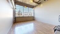 Located at 2320 E Superior Ave in Cleveland, OH, this striking three-bedroom, three-bathroom loft blends industrial heritage with modern functionality. The open living area commands attention with soaring ceilings, exposed concrete, visible ductwork, and expansive factory-style steel-framed windows that flood the space with natural light and offer sweeping urban views. Industrial pendant lighting complements the raw architectural character throughout.

The kitchen features rich, dark wood cabinetry paired with granite-look countertops, stainless steel appliances including a range and dishwasher, and a large window above — all set against the dramatic double-height backdrop. Warm hardwood-style flooring runs consistently throughout the living areas and bedrooms, creating a cohesive, inviting ambiance.

Each of the three bedrooms offers a neutral color palette, hardwood flooring, and dedicated closet space with built-in rods. The spacious primary bedroom provides a generous layout well-suited for comfortable living. The three bathrooms are cleanly finished with walk-in shower stalls featuring chrome fixtures, neutral tile flooring, and white vanities with large mirrors and overhead lighting. A connecting hallway ties the private quarters together efficiently, making this a well-organized and characterful urban residence.