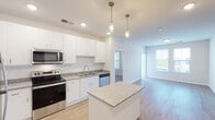 This single-floor residence offers a thoughtfully designed open-concept layout that seamlessly connects the kitchen and living areas. The kitchen serves as the heart of the home, showcasing crisp white shaker cabinetry, granite countertops, a full suite of stainless steel appliances including a refrigerator, electric range, microwave, and dishwasher, along with a central island with additional counter space. Stylish pendant lighting adds a refined touch above the island. Light hardwood-style flooring runs throughout the main living and kitchen areas, creating a warm, cohesive aesthetic. The living area benefits from natural light courtesy of multiple windows with blinds. Bedrooms are finished with plush carpeting and feature generous windows that bring in outdoor views. The bathrooms are well-appointed with granite-topped vanities, undermount sinks, and walk-in closet access, with one bathroom offering a shower/tub combination. A dedicated in-unit laundry closet equipped with a front-loading washer adds everyday convenience. The space also includes a private entry door and ample storage throughout, making it a complete and functional residence.