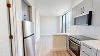 Located at 1559 Northwest 15th Street Road in Miami's vibrant Allapattah neighborhood, this thoughtfully designed unit offers a efficient single-floor layout comprising a kitchen, living area, bedroom, and full bathroom. Light wood-tone flooring runs throughout, lending warmth and visual continuity to the space.

The kitchen is a standout feature, outfitted with sleek slate-blue cabinetry, white countertops, a stainless steel refrigerator, electric range, built-in microwave, and an undermount sink. A peninsula counter extends the workspace and subtly defines the transition into the living area, which benefits from floor-to-ceiling windows that frame urban views of the Miami skyline and flood the space with natural light.

The bedroom is bright and airy, featuring a ceiling fan and a window with an exterior view of lush greenery, enhancing the sense of openness.

The bathroom is well-appointed with a white vanity, large wall mirror, tiled tub-shower combination with a glass sliding door, and recessed lighting. A stacked in-unit washer and dryer is conveniently integrated into the bathroom, adding practical functionality. The overall aesthetic is clean, contemporary, and move-in ready.