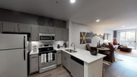 Located on South Lamar Boulevard in Austin's vibrant 78704 zip code, this single-floor unit blends contemporary design with eclectic character. The open-concept layout connects the kitchen, dining, and living areas seamlessly, creating a cohesive and functional flow throughout the space.

The kitchen is outfitted with grey cabinetry, white quartz countertops, a mosaic tile backsplash, and stainless steel appliances including a range, microwave, refrigerator, and dishwasher. A peninsula with bar seating extends into the dining area, offering a casual spot for meals or conversation.

The living room is bright and inviting, featuring crown molding, wood-look flooring, and sliding glass doors that open to an outdoor view of mature trees and a pool area, allowing generous natural light to fill the space.

The bedrooms are well-appointed, each with wood-look flooring and ample natural light from large windows with sheer curtains. One bedroom features a striking exposed brick accent wall paired with pendant lighting, adding an industrial-chic element. Walk-in closet access is visible in this room as well.

The bathroom includes a soaking tub with a tiled surround featuring a bold checkered pattern, a grey vanity, and a large mirror. Throughout the unit, wood-look flooring, recessed lighting, and ceiling fans contribute to a polished, comfortable aesthetic.