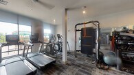 Located at 450 Perimeter Dr in Midlothian, Virginia, this modern fitness center is designed to support a comprehensive range of workout routines. The space is housed on a single floor and finished with durable, patterned carpet tiles that lend a clean, contemporary aesthetic throughout.

The cardio zone is positioned near large windows that invite ample natural light and offer views of the outdoor area, creating an energizing environment for exercise. This section is equipped with multiple treadmills, elliptical cross-trainers, and a stair climber, providing a variety of options for cardiovascular training.

A dedicated strength training area features a multi-station cable and functional training rig with resistance attachment points, ideal for dynamic, full-body workouts. Complementing this is a selection of Matrix-brand selectorized weight machines, including seated cable and leg press units, suitable for targeted muscle conditioning.

Full-length mirrors are strategically placed along the walls to expand the visual space and allow users to monitor their form. A well-stocked dumbbell rack lines one wall, offering a broad range of free weight options. Stability balls and resistance accessories are also available throughout the space.

Structural columns are integrated into the layout, and recessed and pendant lighting fixtures provide consistent illumination. The fitness center is accessed via a glass-paneled door, and the overall design reflects a well-appointed, amenity-grade facility.
